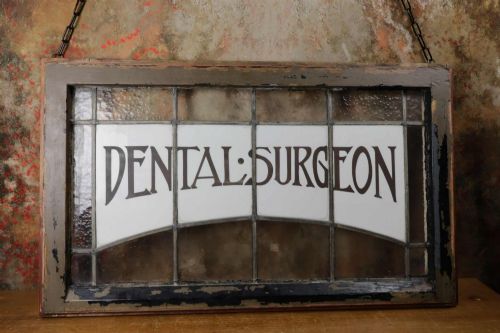 fig 2. An Edwardian leaded glass window panel set in a dark wooden frame with white glass panes featuring black lettering that reads DENTAL SURGEON.