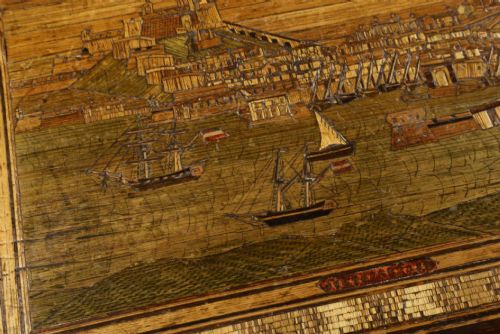 fig 3. A rectangular wooden box top featuring intricate straw marquetry depicting a harbour landscape with ships, fortresses, and geometric borders.