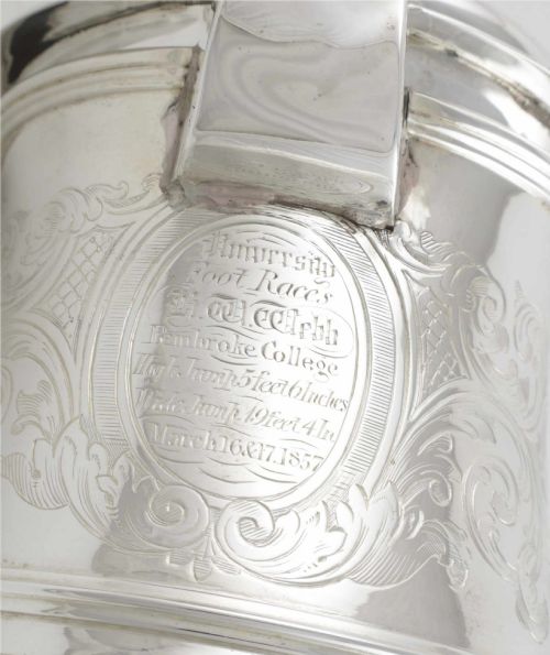 fig 1. An engraved silver lidded jug featuring a hinged cap, scrolling handle, and foliate engraving across the body.