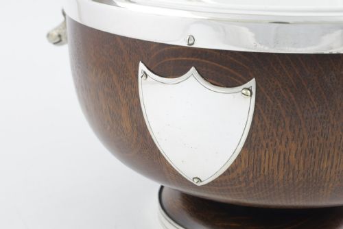 fig 3. A turned dark oak bowl featuring a silver-plated rim, cast stag head handles, a central vacant silver shield, and matching serving utensils.