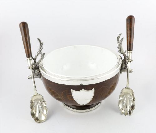 fig 4. A turned dark oak bowl featuring a silver-plated rim, cast stag head handles, a central vacant silver shield, and matching serving utensils.