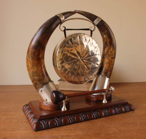 fig 1. A Victorian dinner gong featuring a hammered silver-plated disc suspended between two curved bovine horns mounted on a carved oak base with a striker.