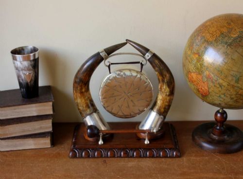 fig 2. A Victorian dinner gong featuring a hammered silver-plated disc suspended between two curved bovine horns mounted on a carved oak base with a striker.
