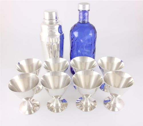 fig 1. A silver-plated Art Deco cocktail shaker accompanied by eight matching conical goblet glasses arranged on a white background.
