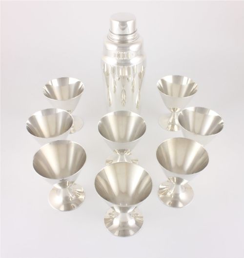fig 2. A silver-plated Art Deco cocktail shaker accompanied by eight matching conical goblet glasses arranged on a white background.