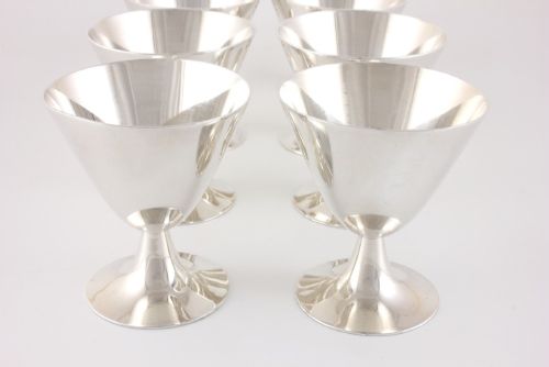 fig 3. A silver-plated Art Deco cocktail shaker accompanied by eight matching conical goblet glasses arranged on a white background.