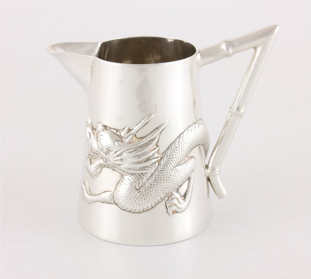 A silver jug with a repousse dragon around the body and a handle shaped like bamboo.