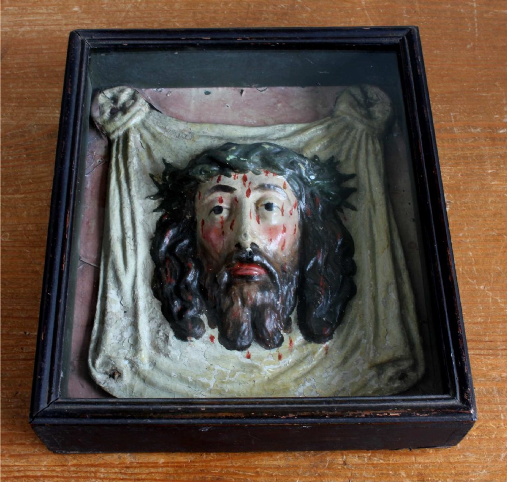 A high-relief polychrome sculpture depicting the Veil of Veronica with the face of Jesus wearing a crown of thorns, presented inside a black glazed wooden shadowbox frame.