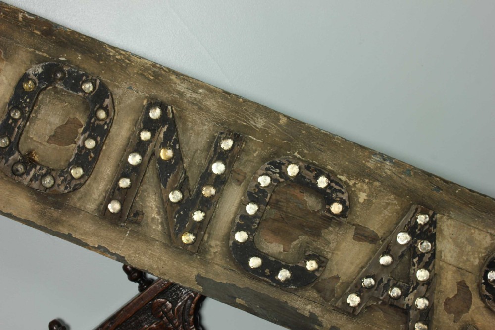 A large, arrow-shaped wooden direction sign painted in weathered cream with the word DONCASTER outlined in raised black lettering set with glass reflectors. View IV