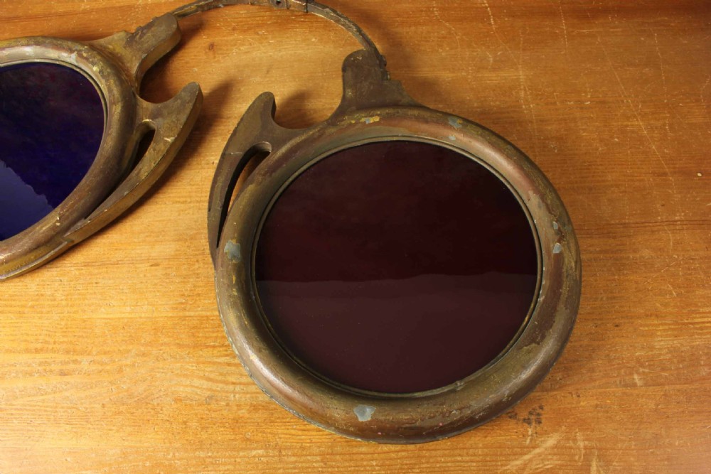 An antique brass optician trade sign in the form of oversized pince-nez spectacles, featuring one red glass lens and one dark blue glass lens. View V