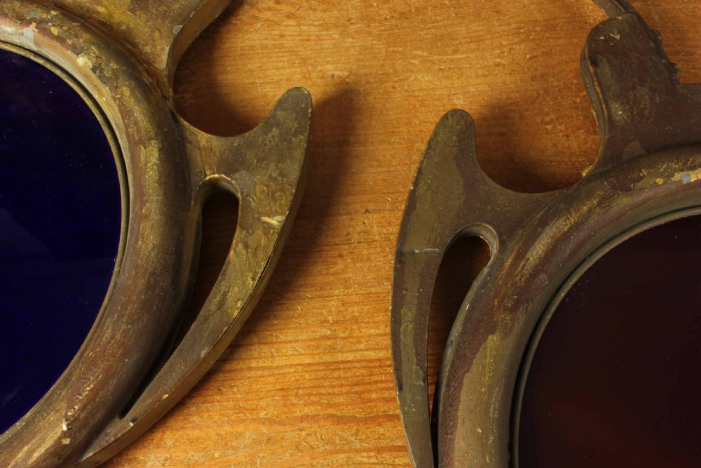 An antique brass optician trade sign in the form of oversized pince-nez spectacles, featuring one red glass lens and one dark blue glass lens. View IX