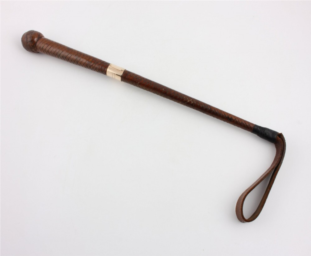 An antique woven dark brown leather riding crop featuring a polished gold collar band and a leather keeper loop at the tip.