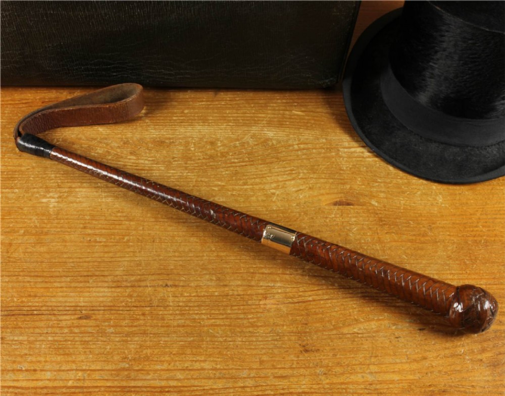An antique woven dark brown leather riding crop featuring a polished gold collar band and a leather keeper loop at the tip. View II