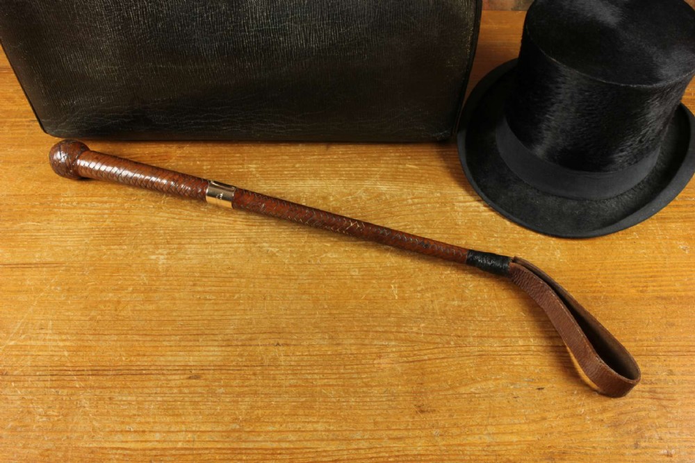 An antique woven dark brown leather riding crop featuring a polished gold collar band and a leather keeper loop at the tip. View III