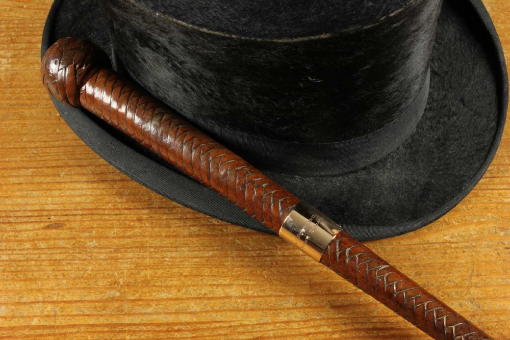 An antique woven dark brown leather riding crop featuring a polished gold collar band and a leather keeper loop at the tip. View X