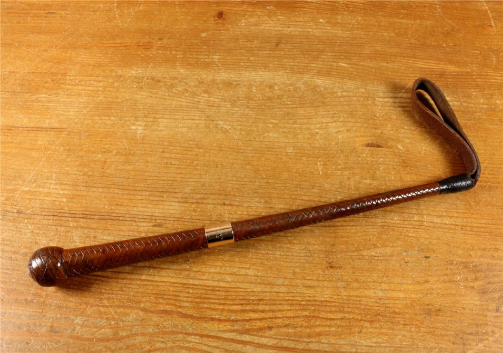 An antique woven dark brown leather riding crop featuring a polished gold collar band and a leather keeper loop at the tip. View XII