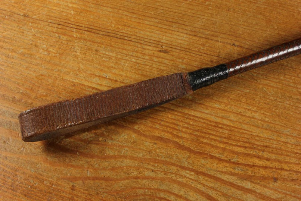 An antique woven dark brown leather riding crop featuring a polished gold collar band and a leather keeper loop at the tip. View XV
