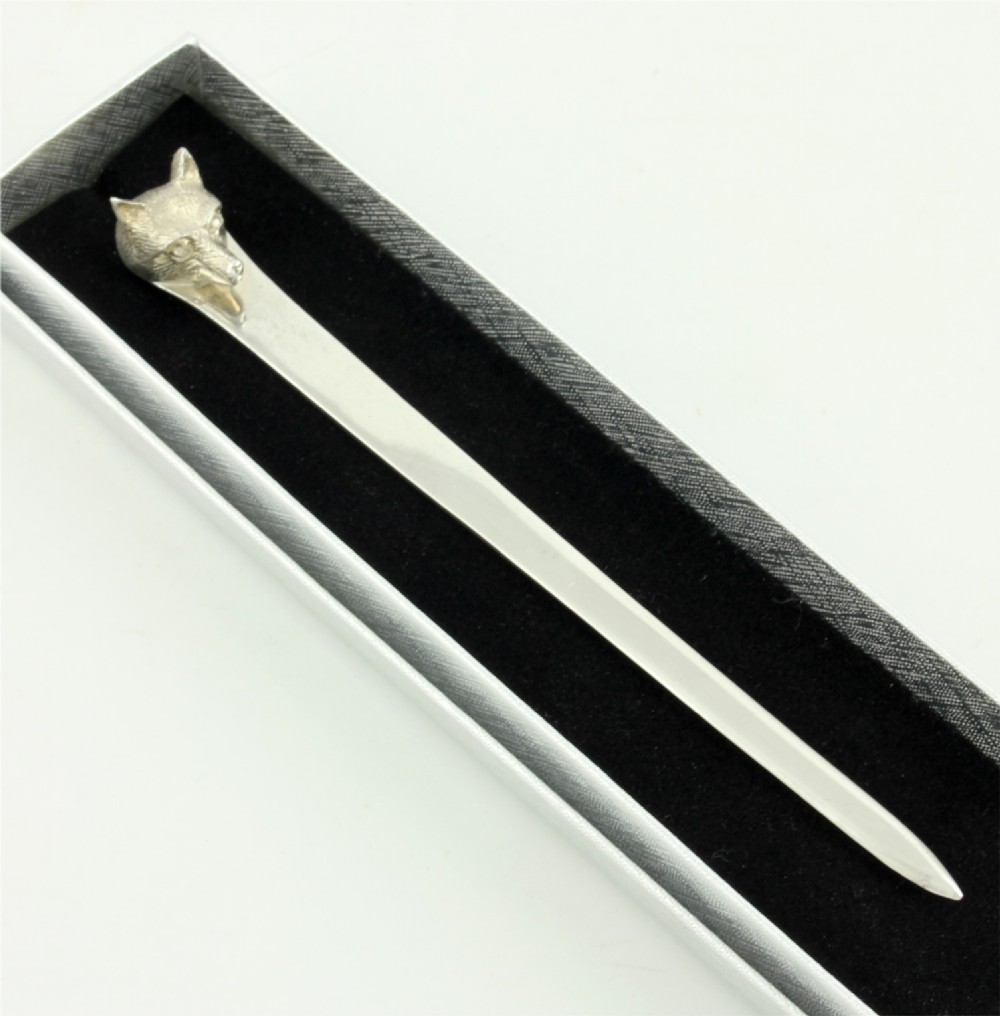 A silver letter opener featuring a sculpted fox head finial atop a smooth, flat tapered blade resting on a brown leather surface. View II