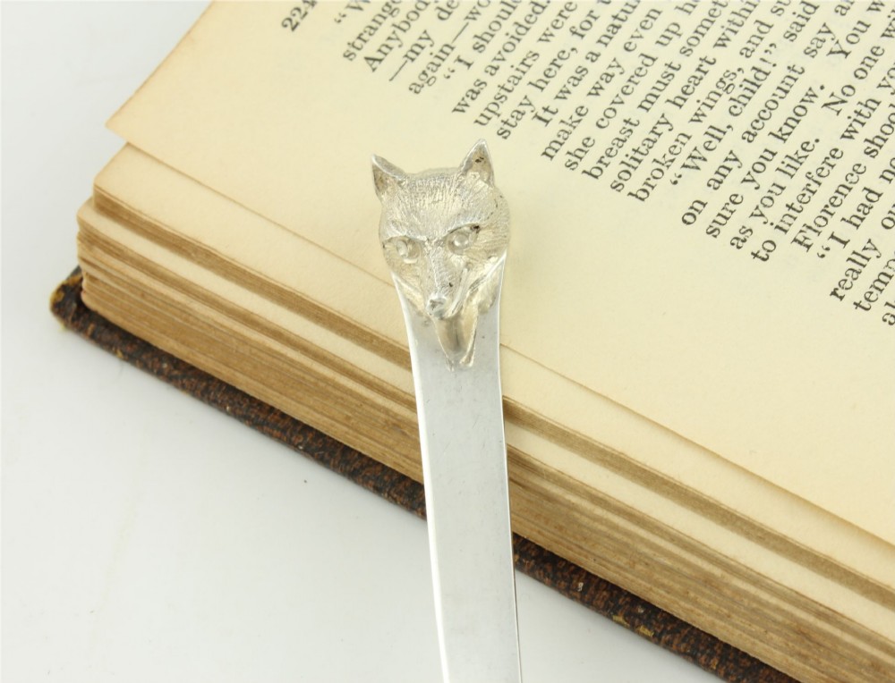 A silver letter opener featuring a sculpted fox head finial atop a smooth, flat tapered blade resting on a brown leather surface. View IV