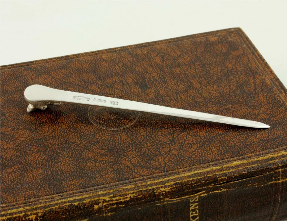 A silver letter opener featuring a sculpted fox head finial atop a smooth, flat tapered blade resting on a brown leather surface. View VI