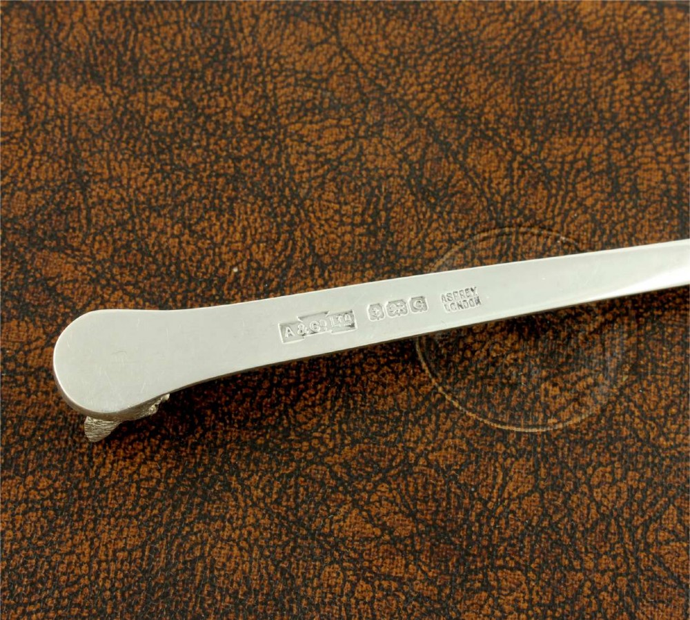A silver letter opener featuring a sculpted fox head finial atop a smooth, flat tapered blade resting on a brown leather surface. View VII