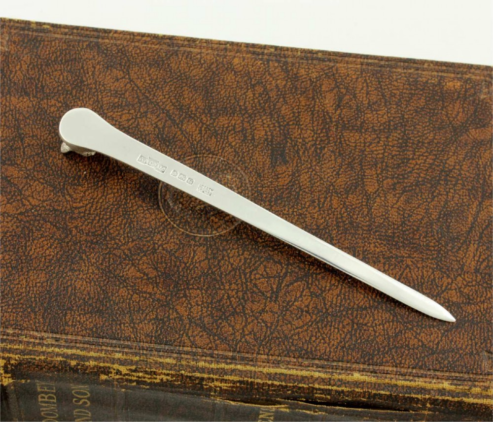 A silver letter opener featuring a sculpted fox head finial atop a smooth, flat tapered blade resting on a brown leather surface. View IX