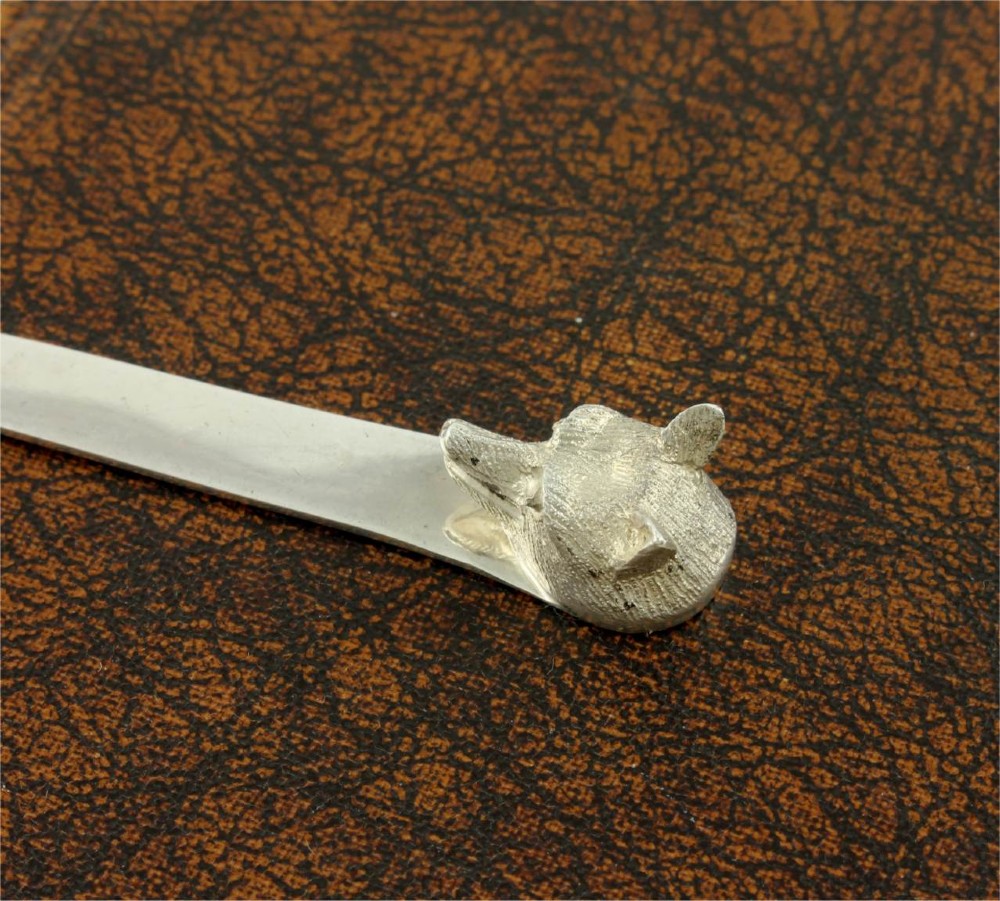 A silver letter opener featuring a sculpted fox head finial atop a smooth, flat tapered blade resting on a brown leather surface. View X
