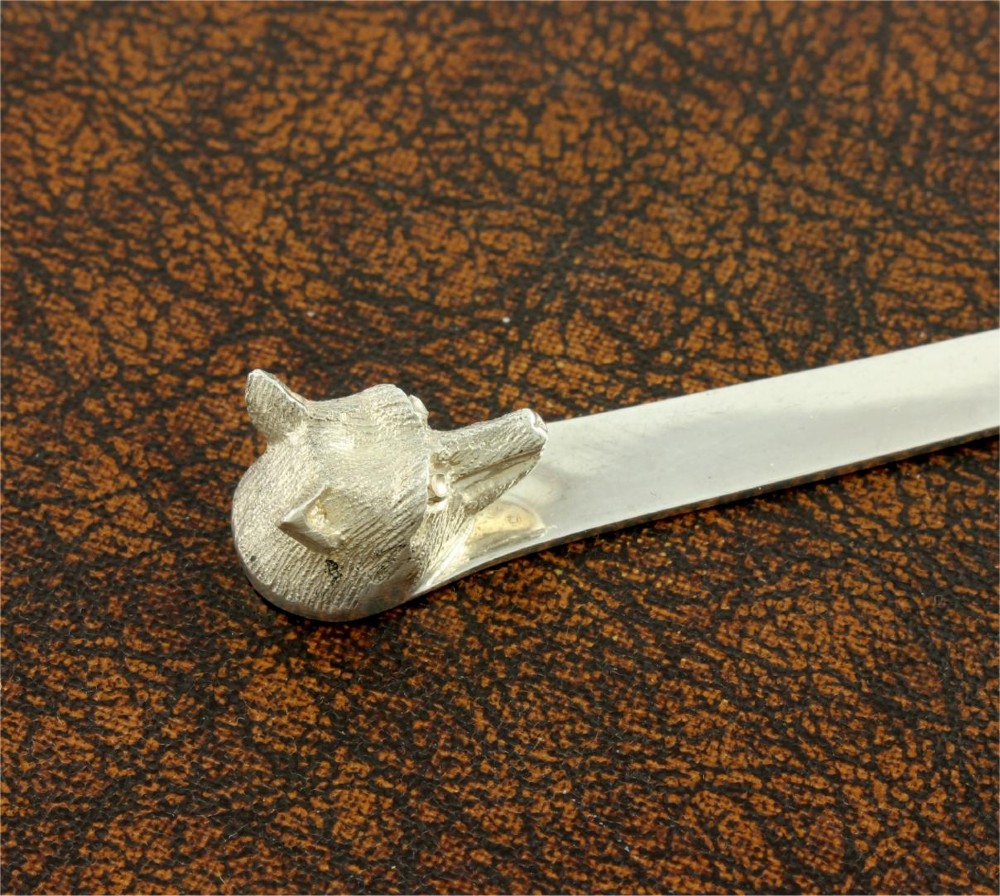 A silver letter opener featuring a sculpted fox head finial atop a smooth, flat tapered blade resting on a brown leather surface. View XIII