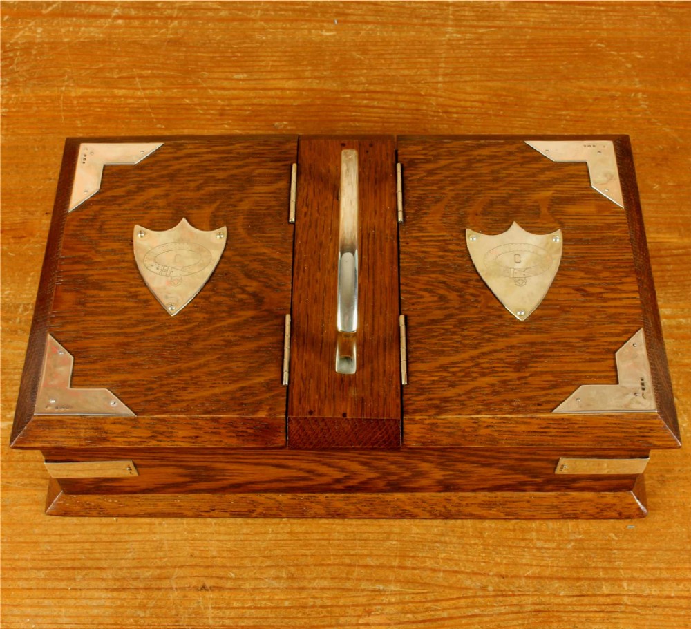 A rectangular dark oak wooden box featuring dual hinged lids, a central metal handle, silver corner mounts, and silver shield motifs on each lid.