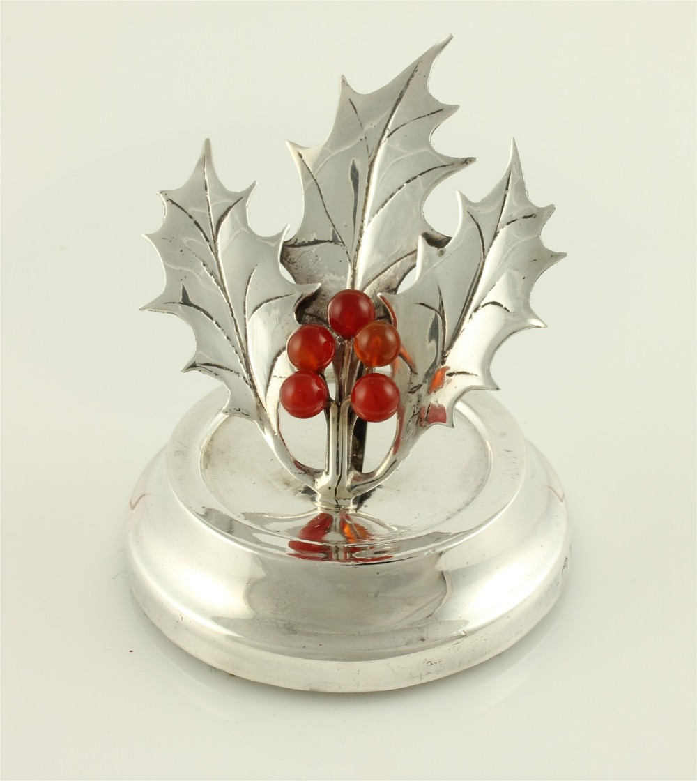 An Edwardian sterling silver menu holder designed as holly leaves with red agate berries set upon a circular stepped base.