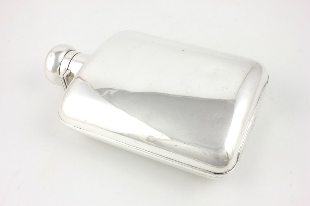 A large, curved silver-plated hip flask featuring a hinged locking cap mechanism and a small attached key against a plain white background. View VIII