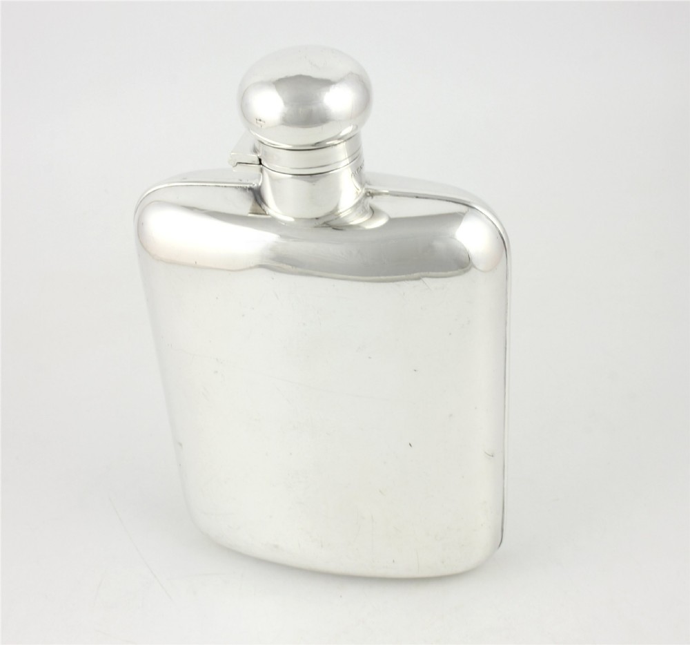 A large, curved silver-plated hip flask featuring a hinged locking cap mechanism and a small attached key against a plain white background. View XIV