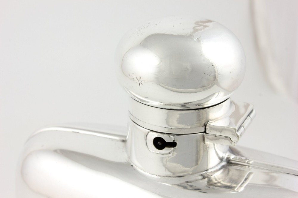 A large, curved silver-plated hip flask featuring a hinged locking cap mechanism and a small attached key against a plain white background. View XV