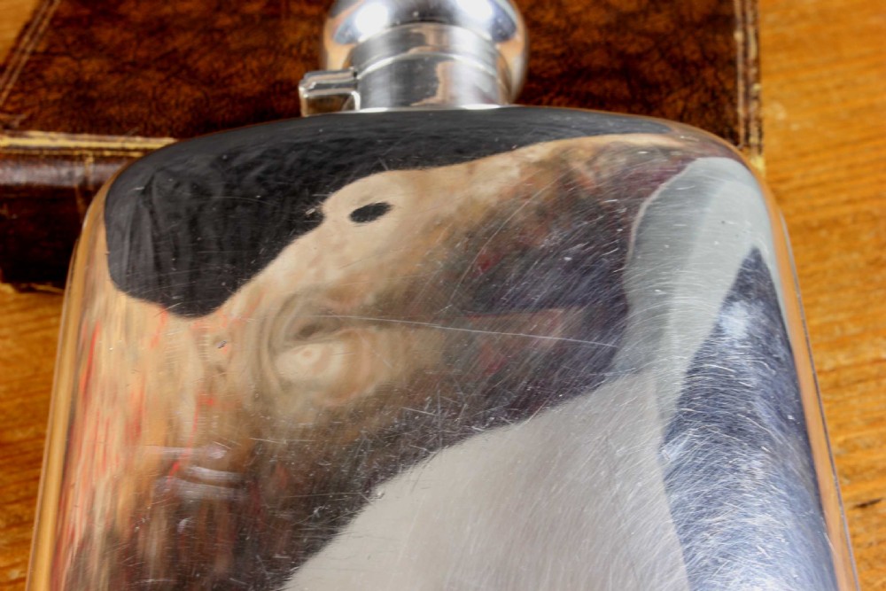 A large, curved silver-plated hip flask featuring a hinged locking cap mechanism and a small attached key against a plain white background. View XVII