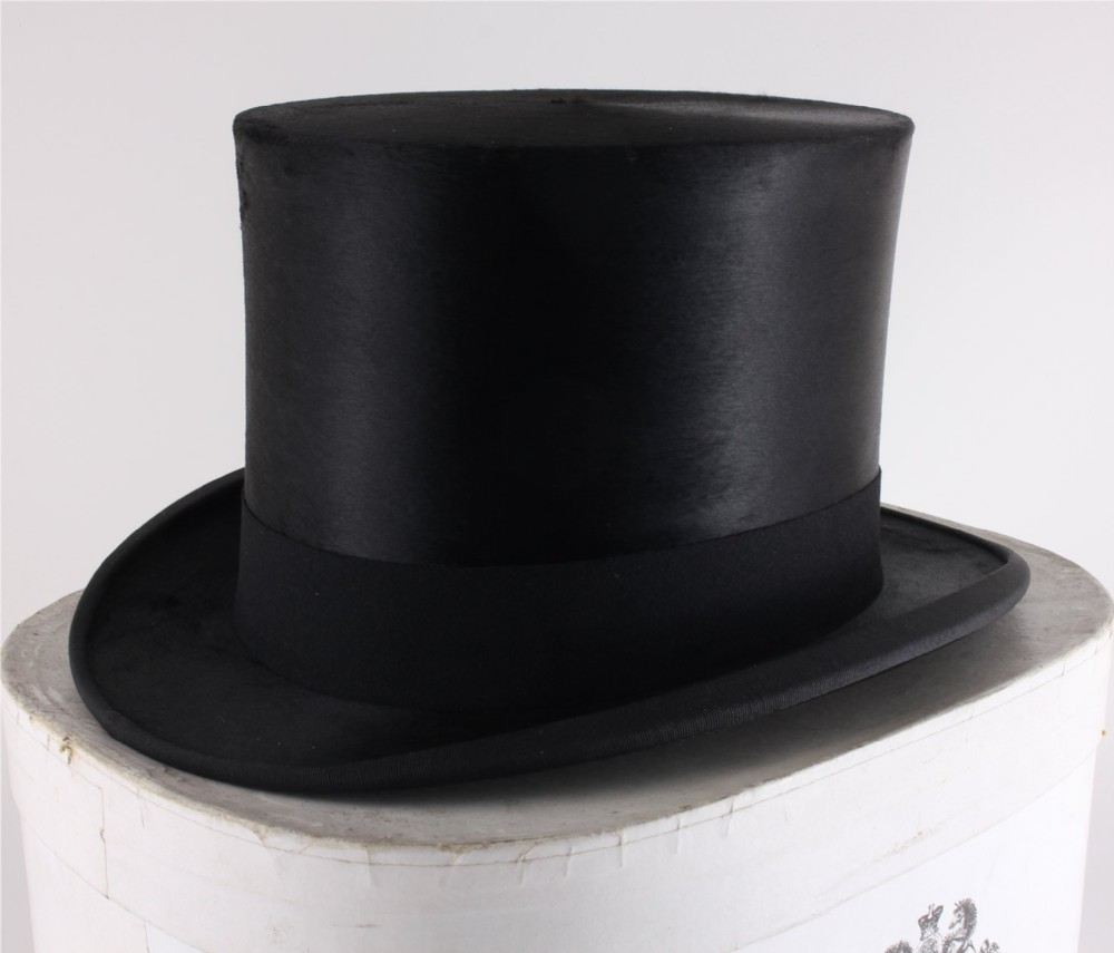 A black silk plush top hat with a grosgrain ribbon band resting on top of an oval hat box.