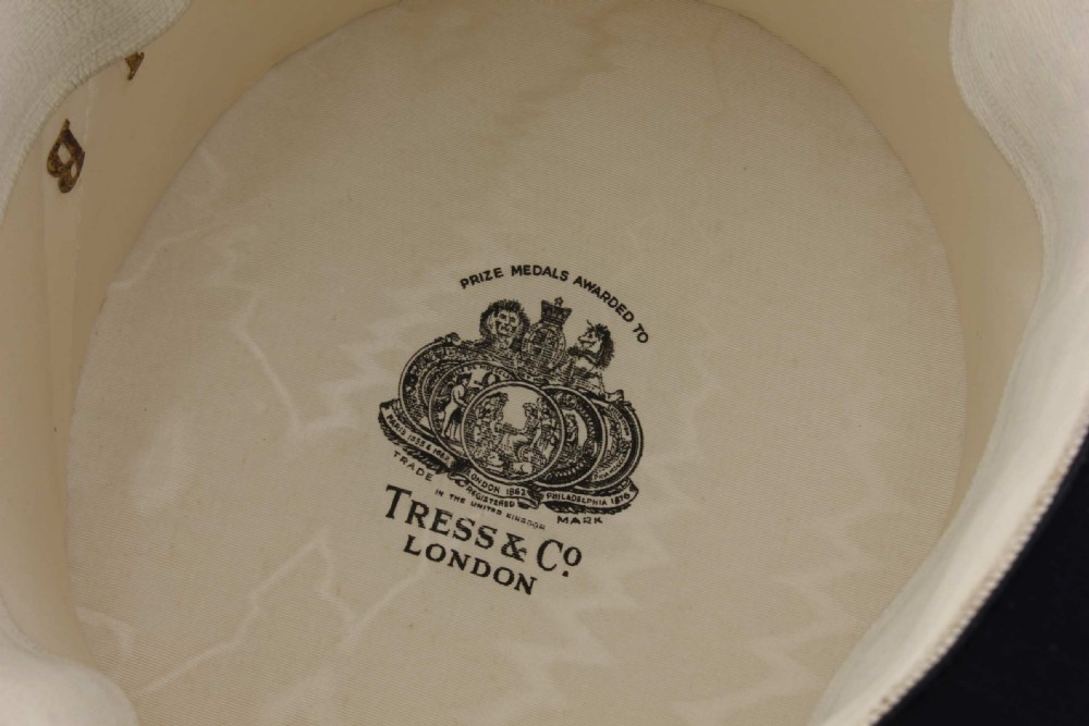 A black silk plush top hat with a grosgrain ribbon band resting on top of an oval hat box. View XIV