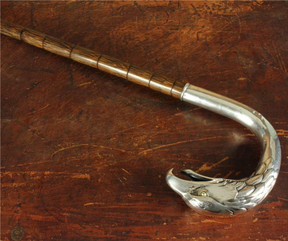An antique walking cane featuring an 800 silver handle sculpted in the shape of an eagle head, mounted on a dark ribbed wood shaft.