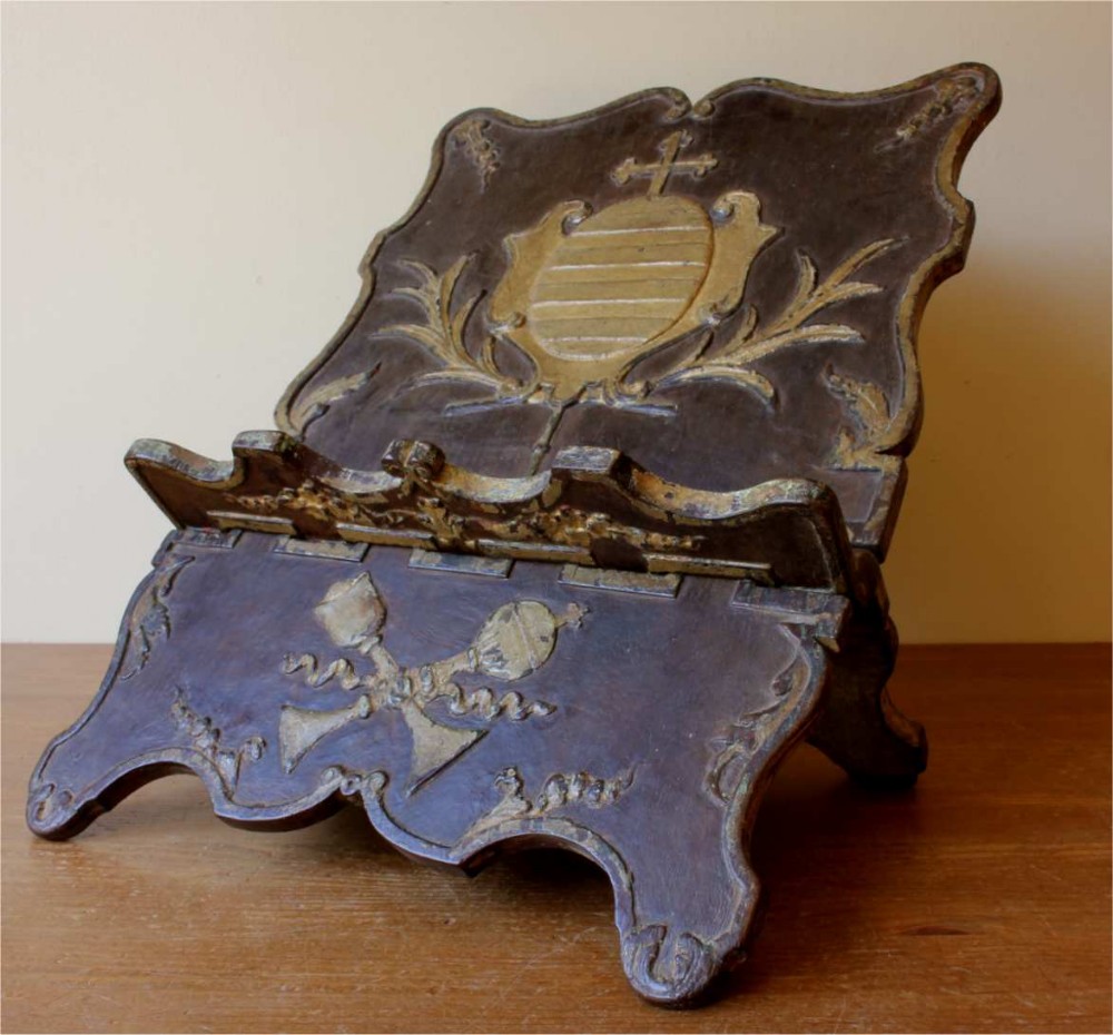 An 18th-century carved wooden folding missal stand featuring a dark finish with gilded heraldic motifs and scalloped edges.