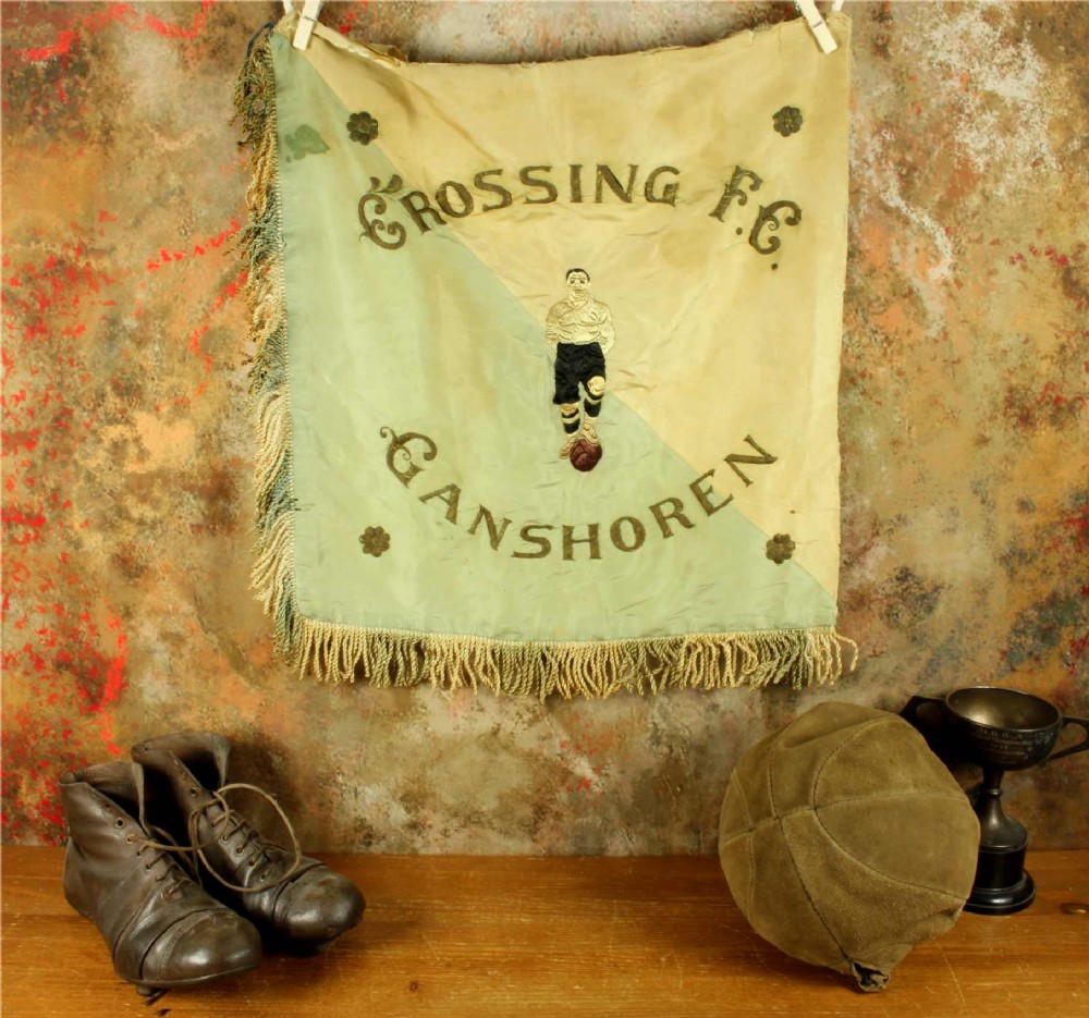 A square two-tone silk banner featuring pale green and cream diagonal panels, embroidered lettering reading Crossing FC Ganshoren, a central footballer figure, and fringe trim. View II