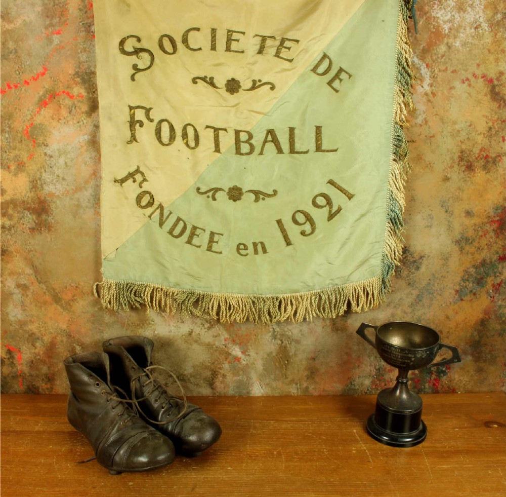 A square two-tone silk banner featuring pale green and cream diagonal panels, embroidered lettering reading Crossing FC Ganshoren, a central footballer figure, and fringe trim. View III