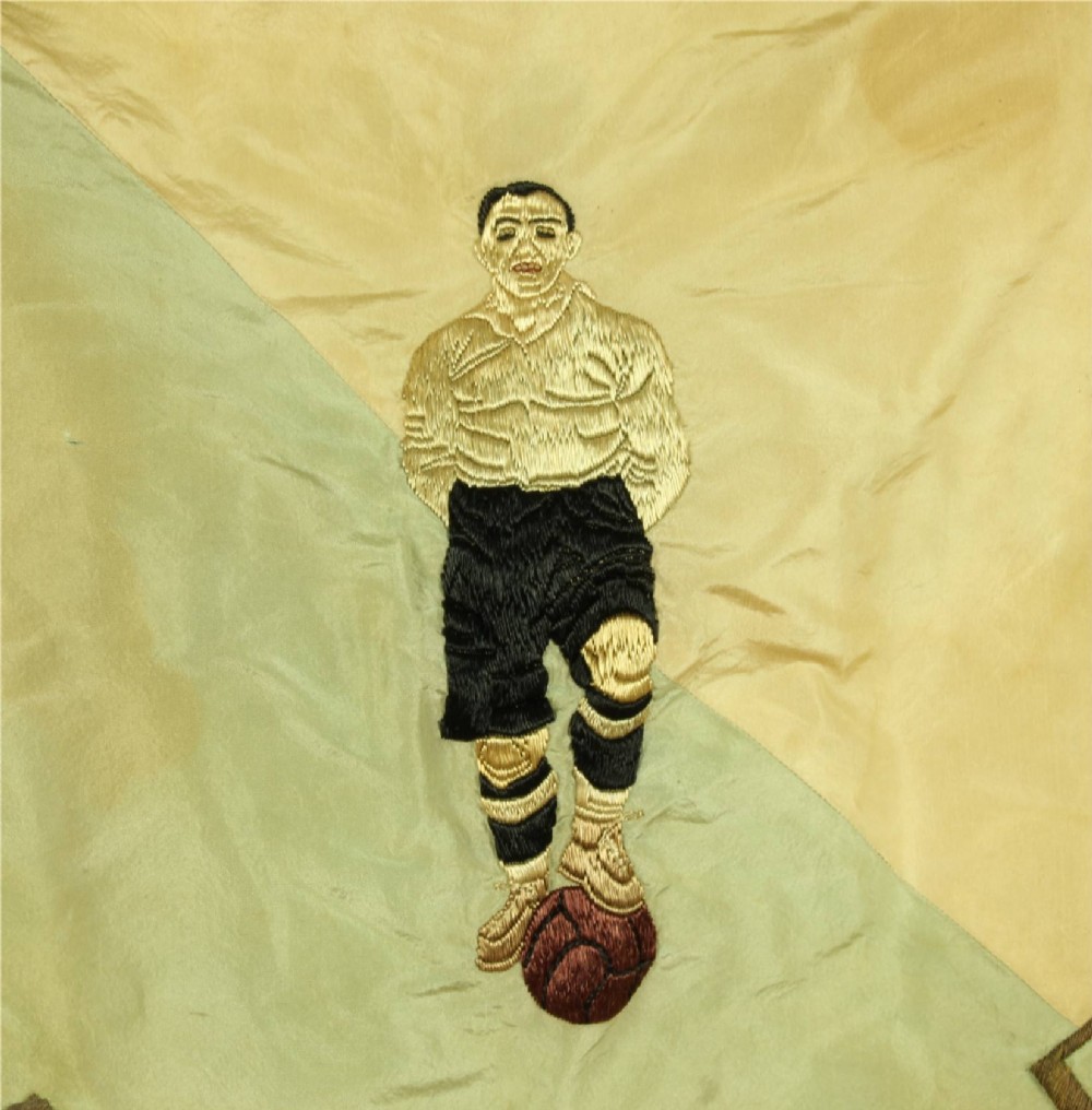A square two-tone silk banner featuring pale green and cream diagonal panels, embroidered lettering reading Crossing FC Ganshoren, a central footballer figure, and fringe trim. View V
