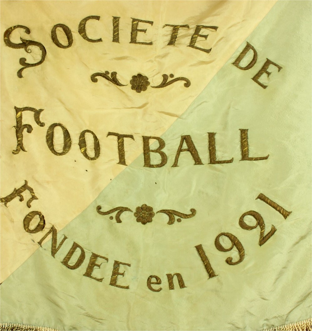 A square two-tone silk banner featuring pale green and cream diagonal panels, embroidered lettering reading Crossing FC Ganshoren, a central footballer figure, and fringe trim. View VI