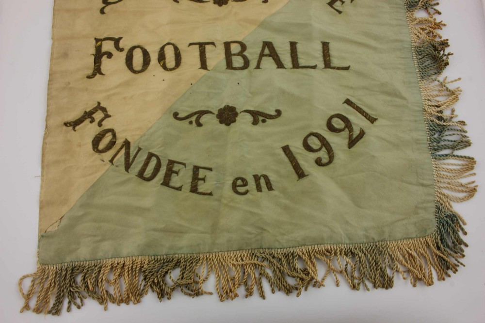 A square two-tone silk banner featuring pale green and cream diagonal panels, embroidered lettering reading Crossing FC Ganshoren, a central footballer figure, and fringe trim. View VII
