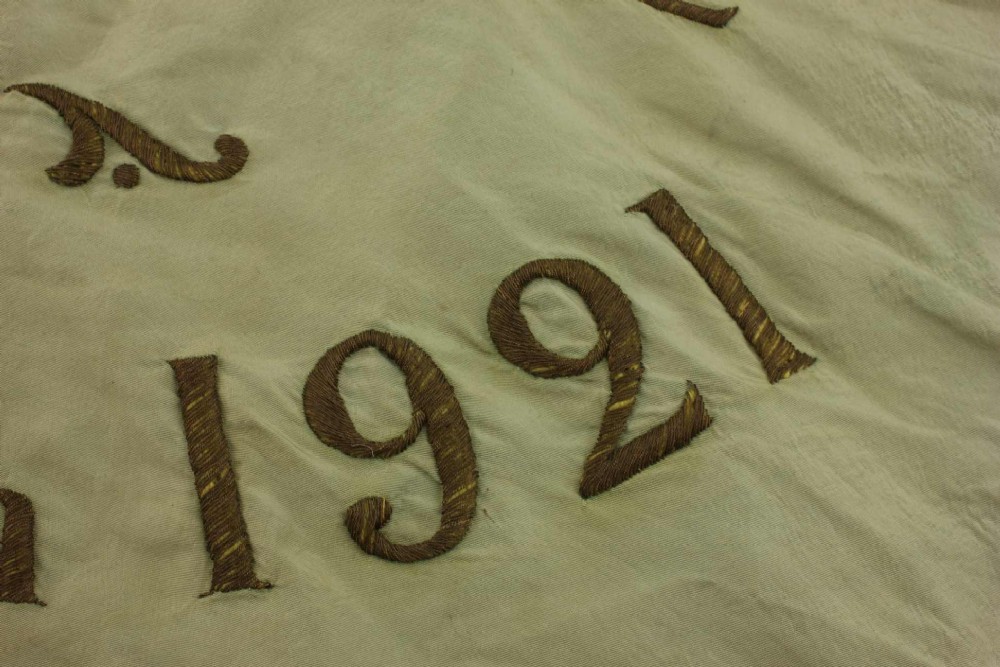 A square two-tone silk banner featuring pale green and cream diagonal panels, embroidered lettering reading Crossing FC Ganshoren, a central footballer figure, and fringe trim. View XI
