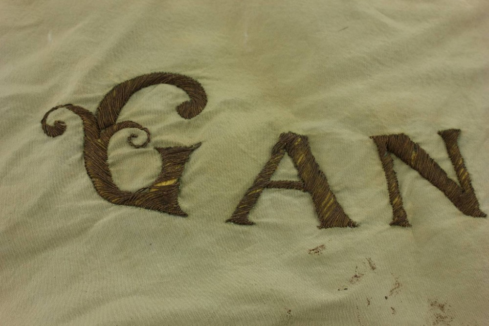 A square two-tone silk banner featuring pale green and cream diagonal panels, embroidered lettering reading Crossing FC Ganshoren, a central footballer figure, and fringe trim. View XII