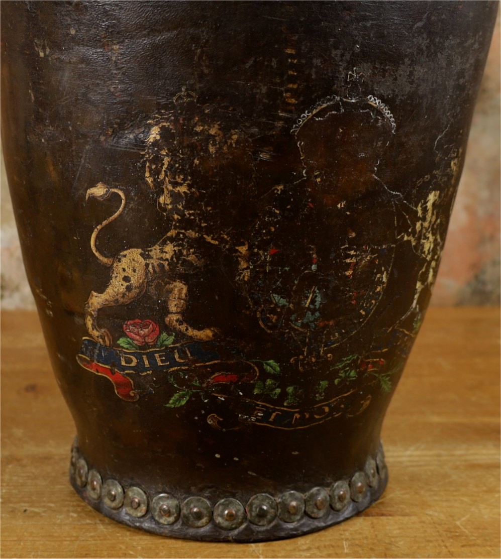 A dark brown Georgian leather fire bucket featuring a heavy strap handle, brass studs around the base, and a painted royal coat of arms with a lion and unicorn. View III