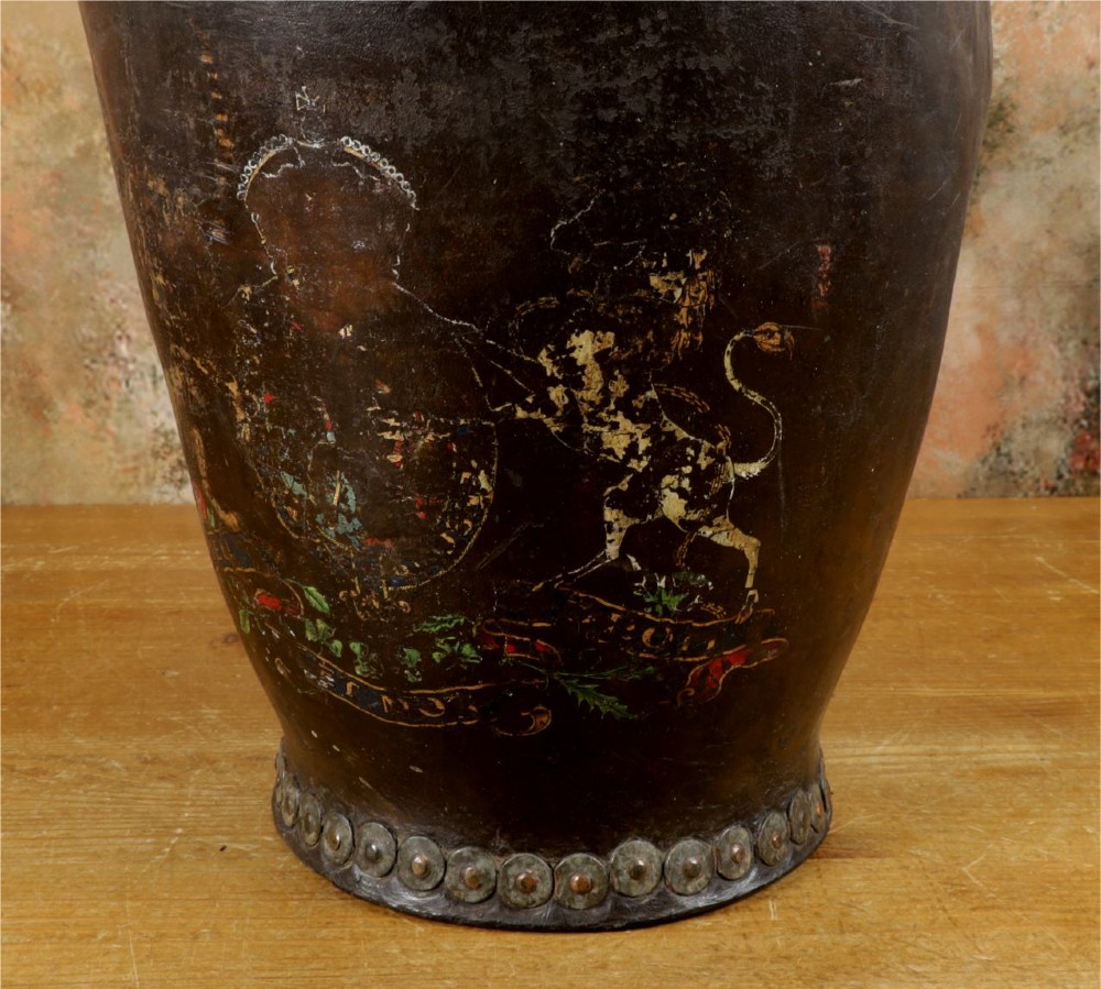 A dark brown Georgian leather fire bucket featuring a heavy strap handle, brass studs around the base, and a painted royal coat of arms with a lion and unicorn. View IV