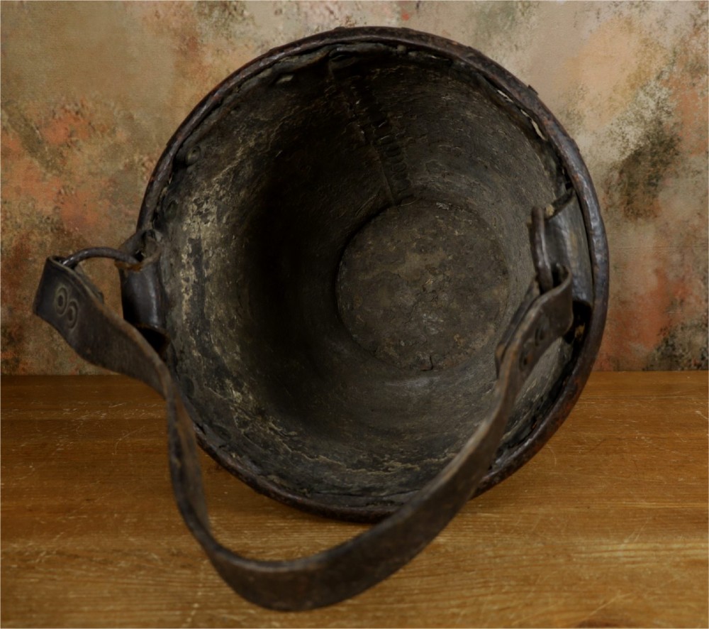 A dark brown Georgian leather fire bucket featuring a heavy strap handle, brass studs around the base, and a painted royal coat of arms with a lion and unicorn. View V