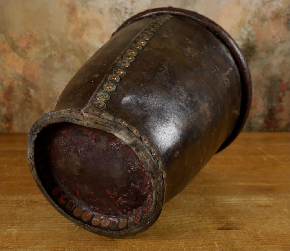 A dark brown Georgian leather fire bucket featuring a heavy strap handle, brass studs around the base, and a painted royal coat of arms with a lion and unicorn. View VI