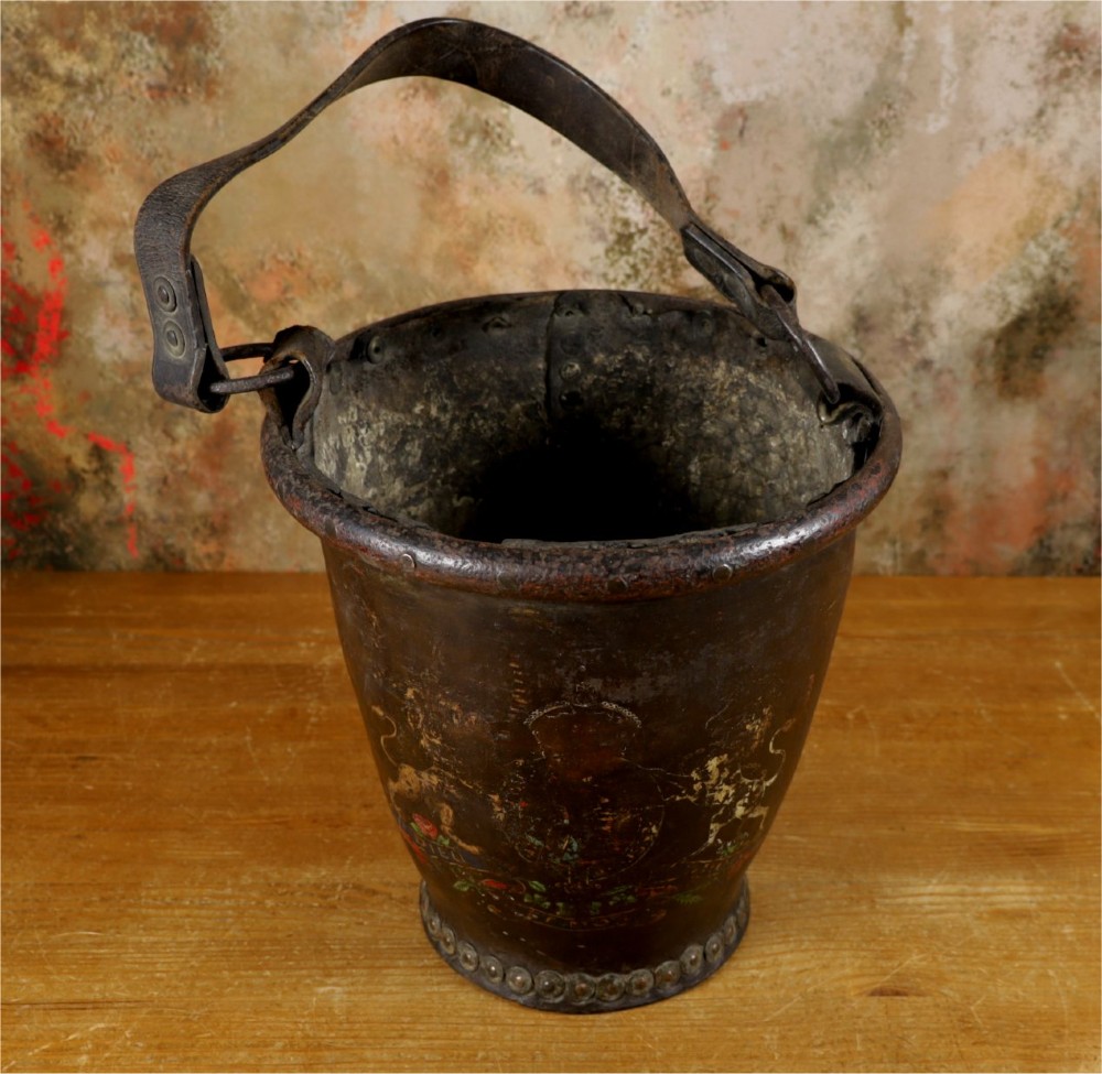 A dark brown Georgian leather fire bucket featuring a heavy strap handle, brass studs around the base, and a painted royal coat of arms with a lion and unicorn. View VII